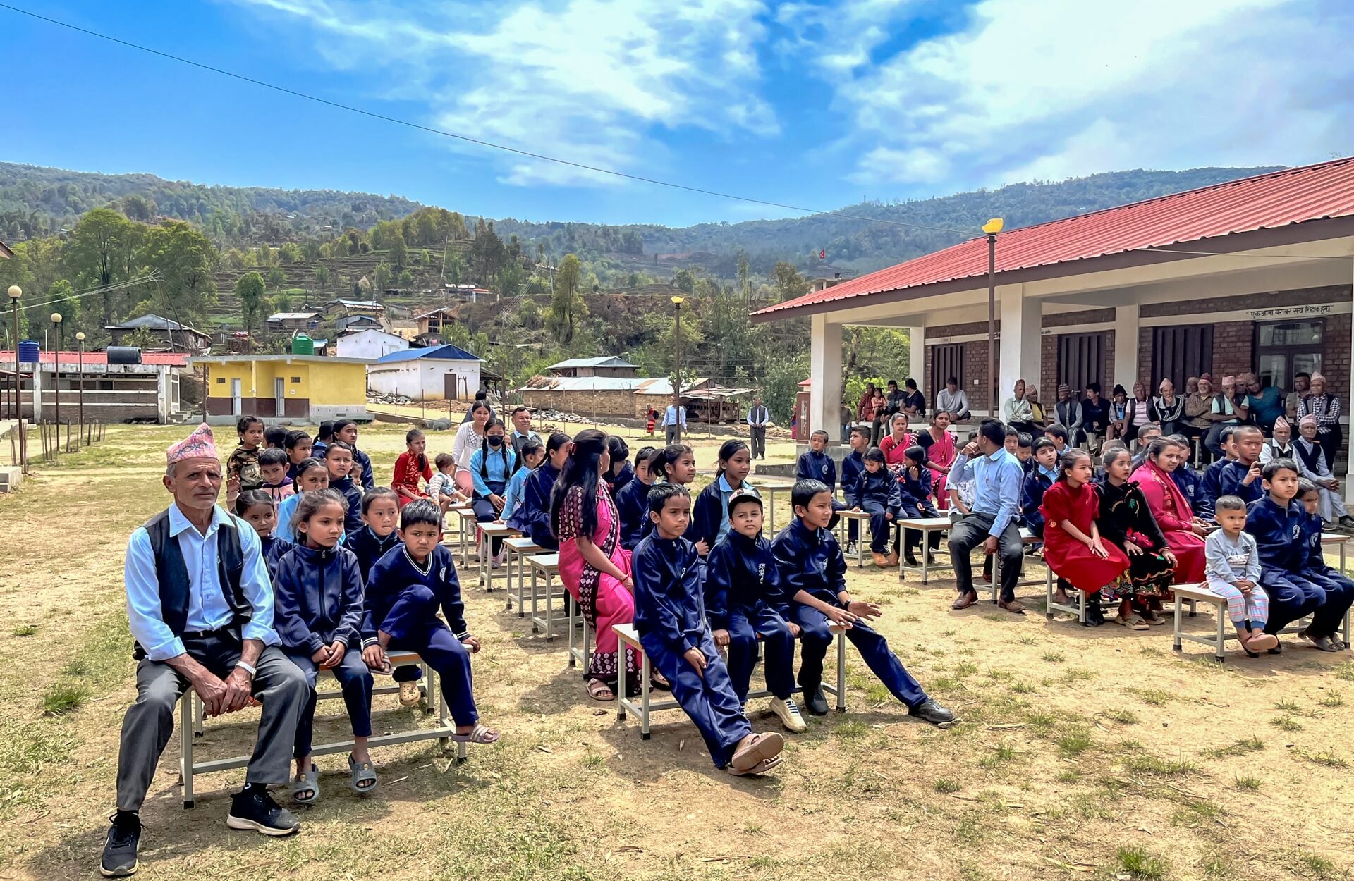 Schulkinder sitzen zu einer Feierlichkeit des Nepalschulprojektes auf dem Schulhof.