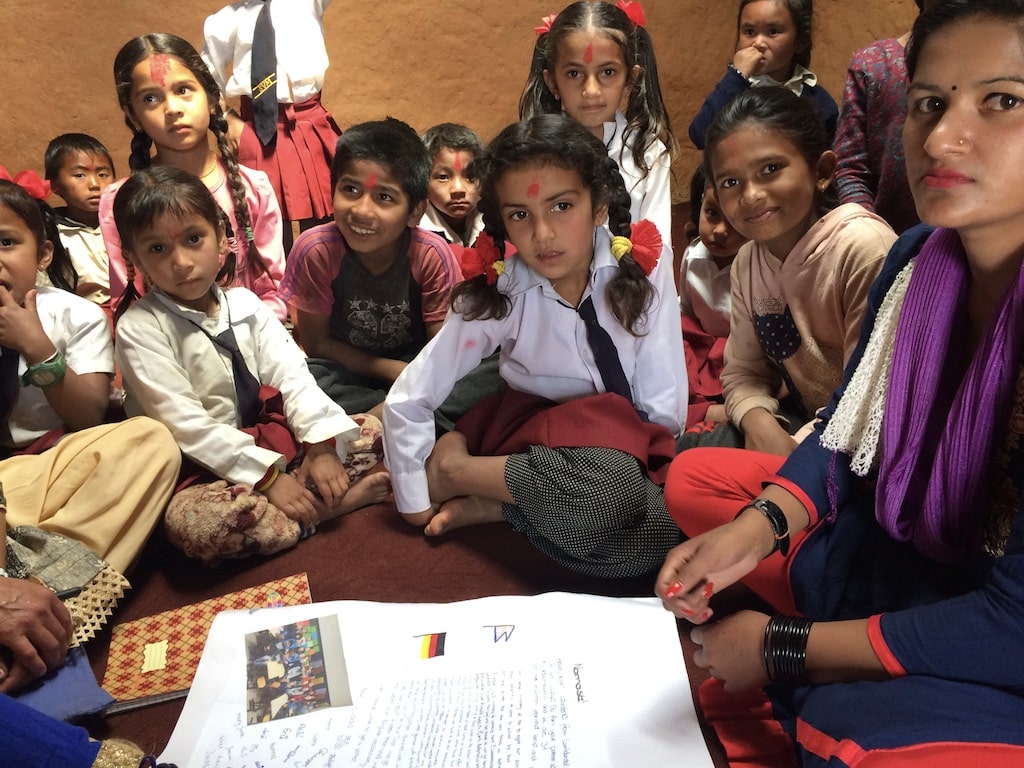 Schulkinder sitzen zu einer Feierlichkeit des Nepalschulprojektes auf dem Schulhof.